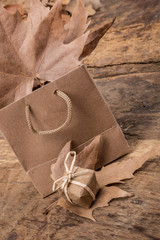 gift, shopping bag and dried leafs on wooden surface