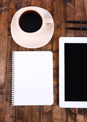 Tablet, cup of coffee, notebook and pens on wooden background