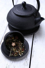 Obraz na płótnie Canvas Black teapot, bowl and tea on color wooden background
