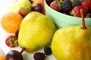 Ripe fruits and berries in bowl on table close up