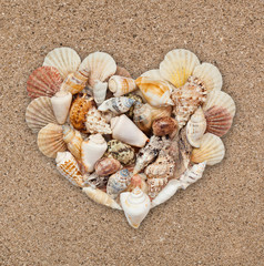 Seashells stacked in the form of heart on the background of sand