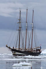 Fototapeta na wymiar Black tourist sailing ship in Antarctic waters clogged with ice