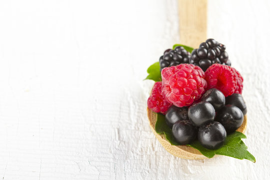 Forest berries in wooden spoon on white wooden table