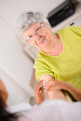 cheerful elderly woman receiving injection from a young nurse