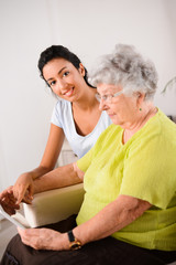 cheerful young girl with elderly woman playing with tablet home