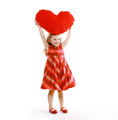 Cheerful charming little curly girl in a dress holding a heart