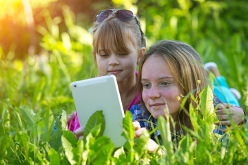 Young sisters with a tablet PC, lying in the grass.