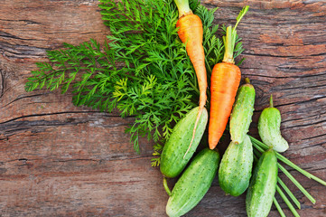Ripe green cucumbers and carrots on old wooden background.