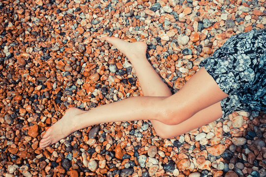 Legs of a young woman on a pebble beach