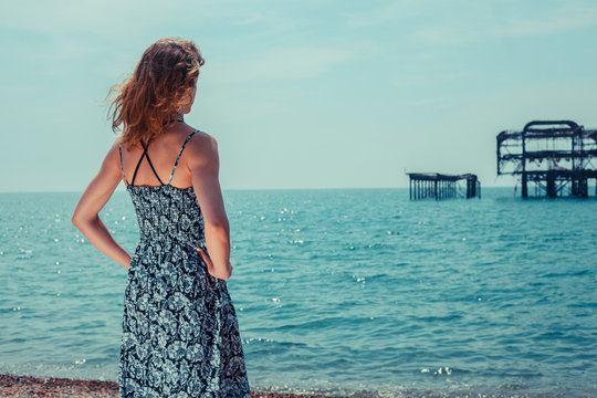 Young woman standing by the ocean with old pier
