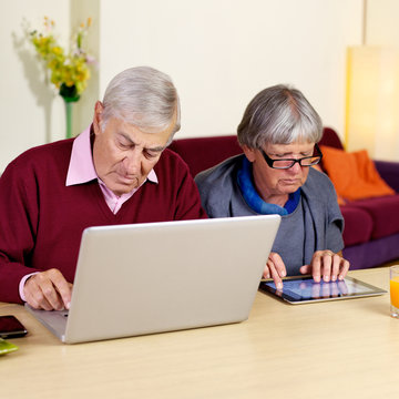 Senior retired couple at home working on pad and pc