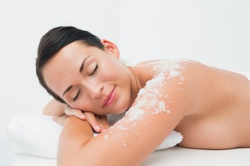 Peaceful brunette lying with salt scrub on shoulders