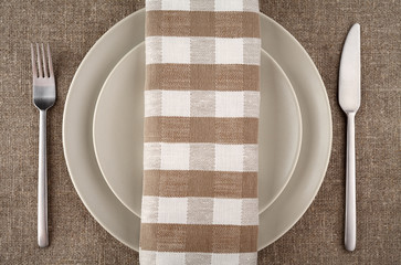 Beige plate, fork, knife and beige linen napkin and tablecloth.