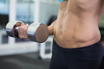 Fototapeta na wymiar Mid section of fit woman exercising with dumbbell in gym