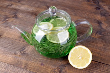 Estragon drink with lemon in teapot on wooden background
