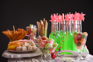 Bottles of drink with straw and sweets on dark background