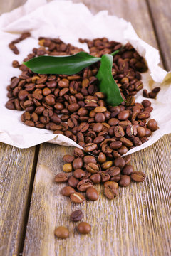 Coffee beans on piece of paper on wooden background