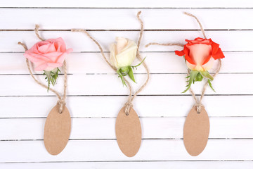 beautiful roses and empty tags on white wooden background