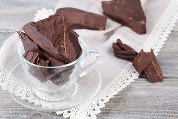 Cracked chocolate bar in glass bowl, on wooden background