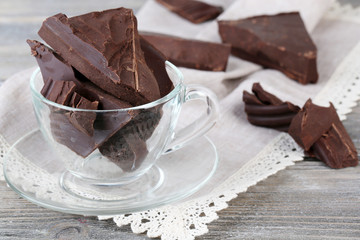 Cracked chocolate bar in glass bowl, on wooden background