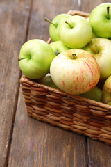 Ripe apples in basket on wooden table close-up