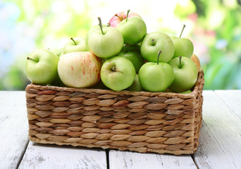 Ripe apples in basket on table on natural background