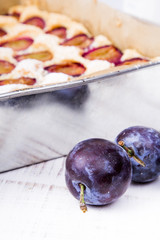 cake with plums on white wooden background