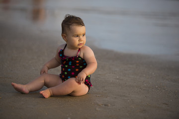 cute baby girl on the beach looking at the sea