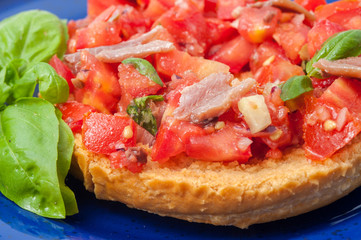 Frisella con pomodori rossi e acciughe su un piatto blu