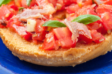 Frisella con pomodori rossi e acciughe su un piatto blu