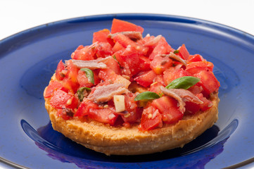 Frisella con pomodori rossi e acciughe su un piatto blu