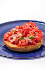 Frisella con pomodori rossi e acciughe su un piatto blu