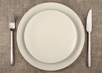 Beige plate, fork, knife and beige linen tablecloth.