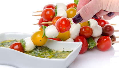 Hand dipping a skewer of cherry tomatoes and mozzarella in a vin