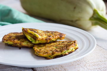 fried zucchini fritters on a white plate,white wooden background