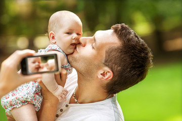 Naklejka premium Family with baby In Park taking selfie by mobile phone