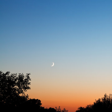 new moon in dark blue and red sky at late sunset