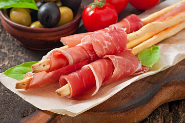 Grissini bread sticks with ham, olives, basil on table
