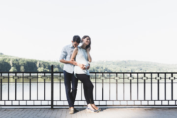 Happy and young pregnant couple hugging in nature at the lake