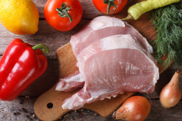 raw pork meat on a cutting board and fresh vegetables top view