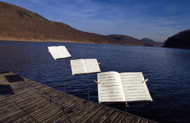 Drei Notenständer hintereinanderstehend auf einem Steg am See