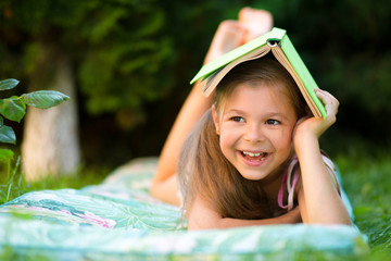 Little girl is hiding under book outdoors