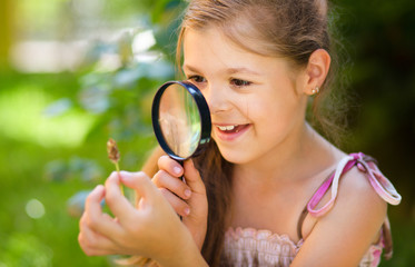 Young girl is looking at flower through magnifier