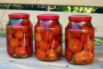 Three glass cans of red tomatoes  on the wooden bench