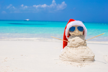 Sandy snowman with red Santa Hat on white Caribbean beach