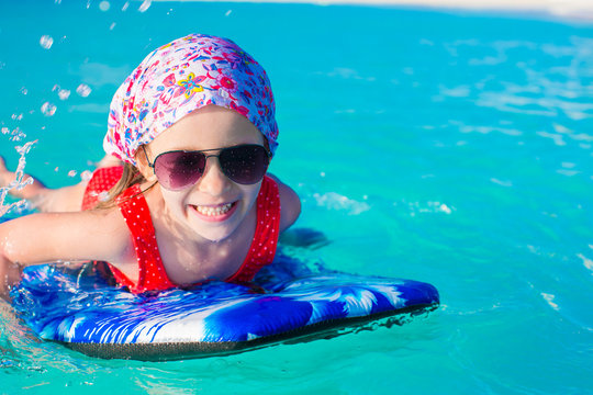 Little adorable girl swimming on surfboard in the turquoise sea