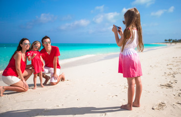 Fototapeta premium Little girl making photo on phone of her family at the beach