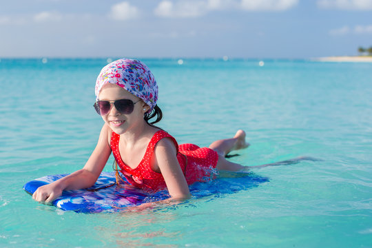 Little cute girl swimming on a surfboard in the turquoise sea