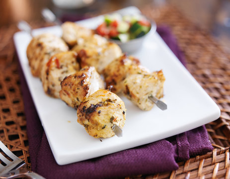 two grilled chicken shishkabob skewers with cucumber salad