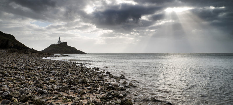 Lighthouse Landscape With Stormy Sky Over Sea With Rocks In Fore